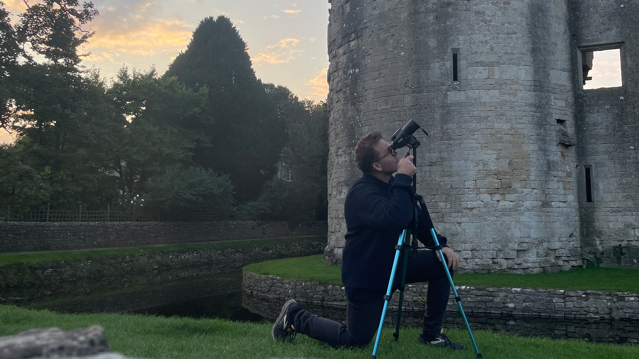 A man looking through a tripod mounted monocular next to a castle.