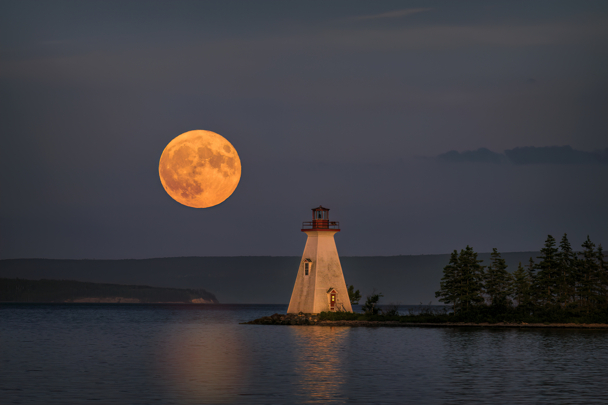 large moon low in sky above a lake.