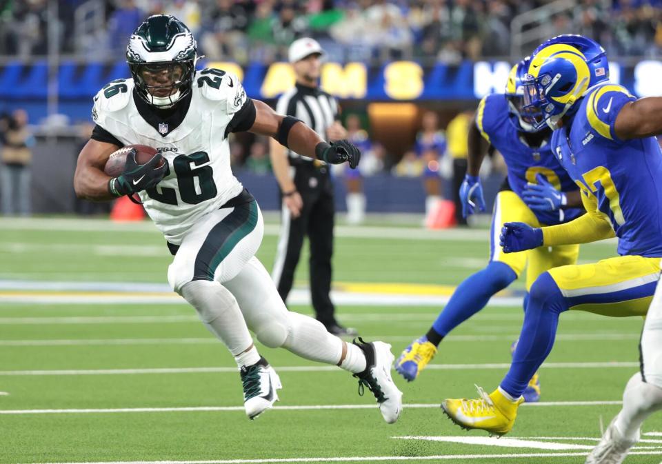 Saquon Barkley, left, runs with the ball past Rams safety Quentin Lake