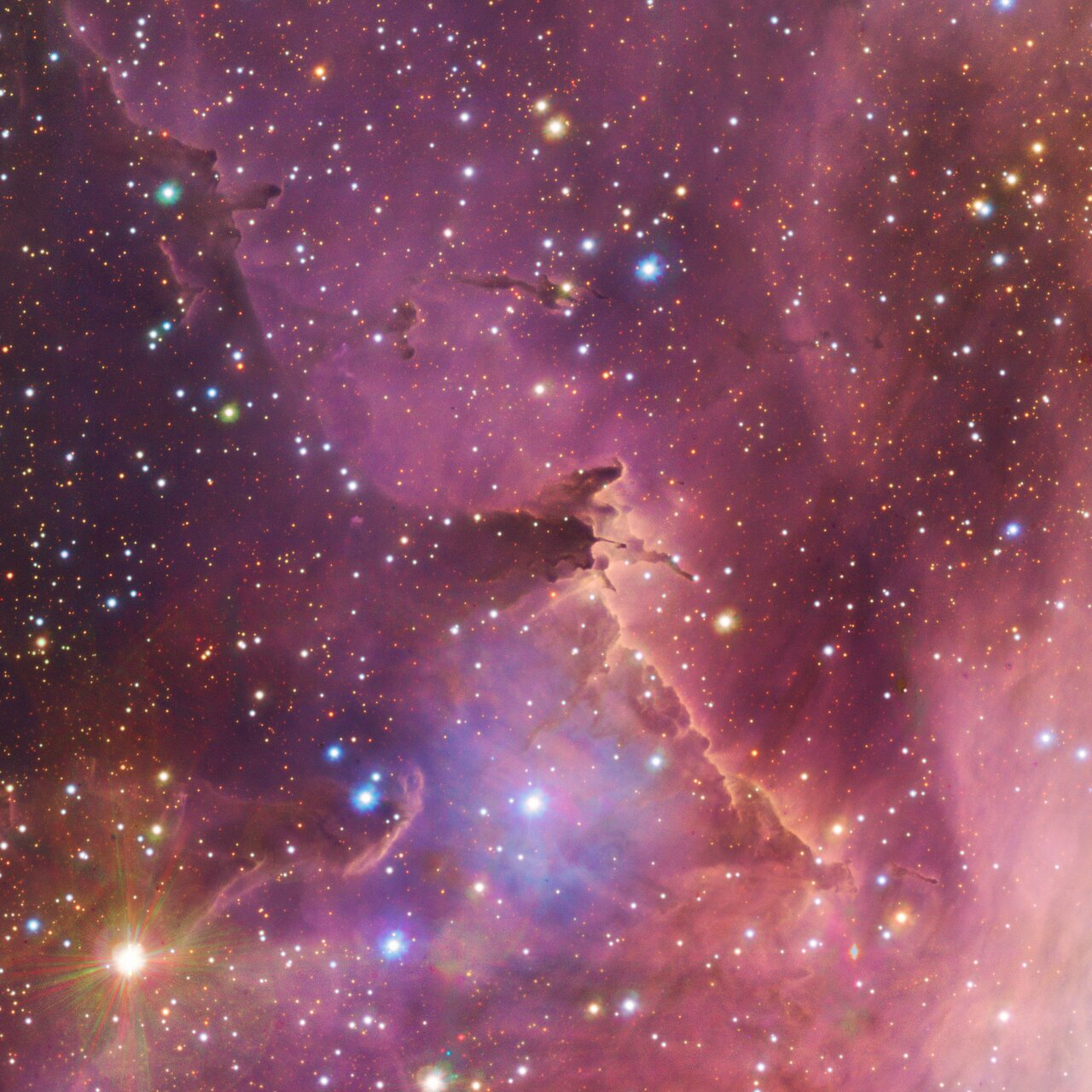 A section of space, awash with pink nebulous clouds, spattered with countless shining points of varying size and color.