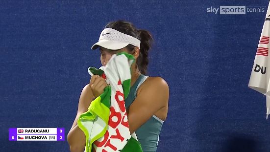 Emma Raducanu wiping her face with a towel after a tennis match.