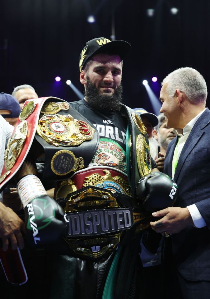 Artur Beterbiev, victorious boxer, wearing championship belts.