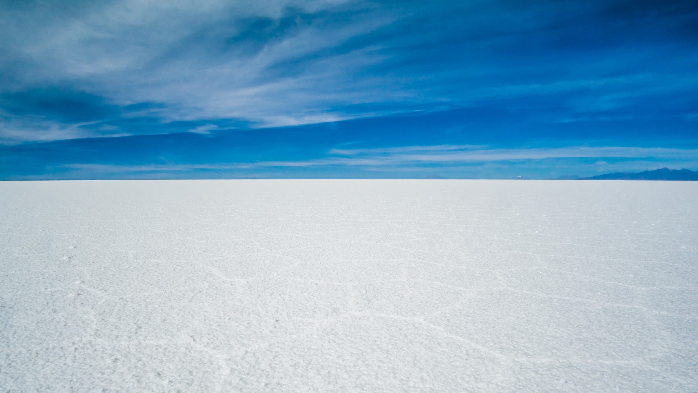 white salt flat in the foreground and a deep blue sky above with a few wispy white clouds.