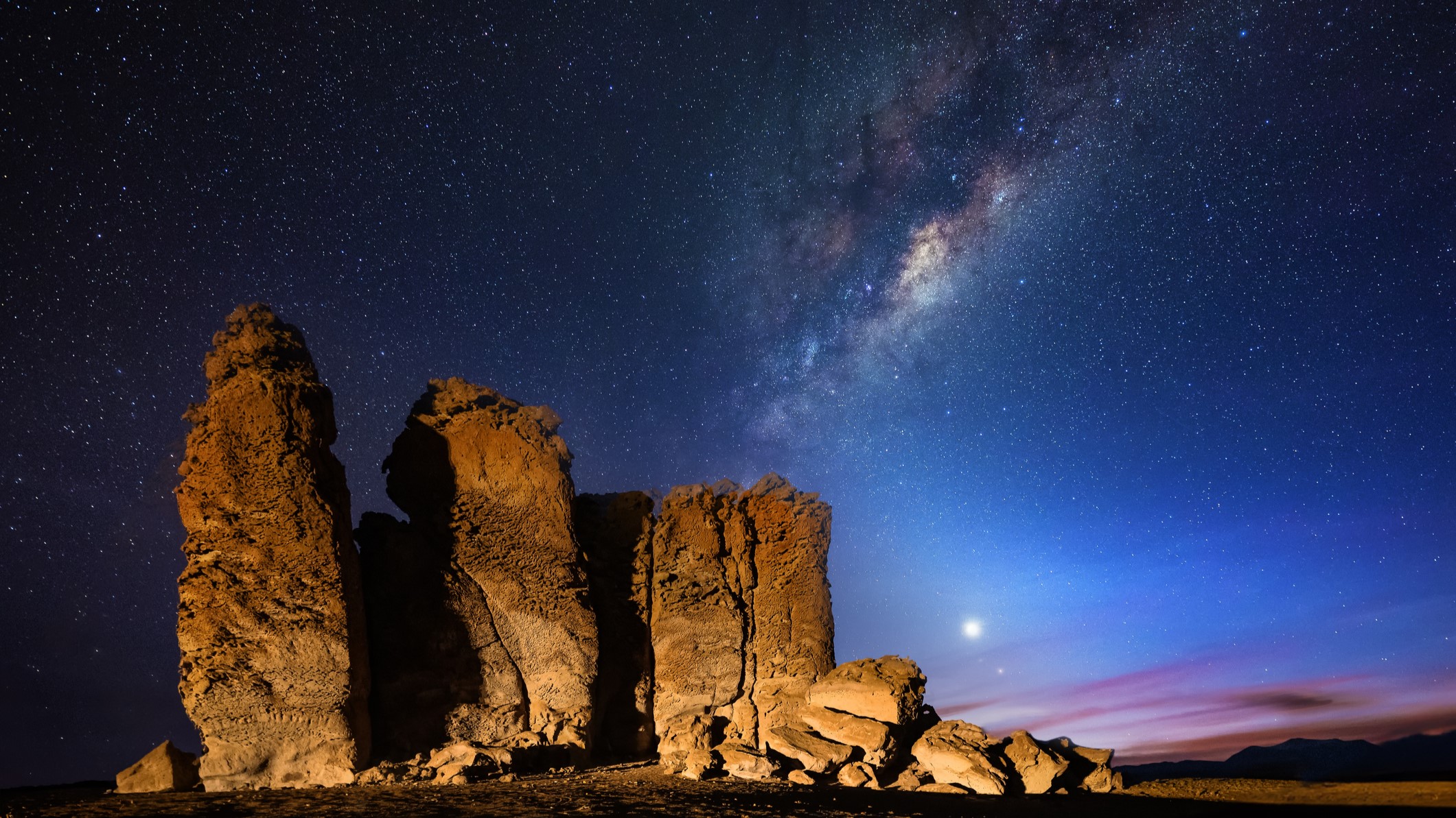 This picture shows a rock formation at the Salar de Tara in front of the Milky way at night. Also on the night sky is the planet venus visible at the horizon.